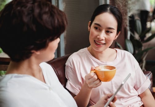 Two women engaging in a friendly conversation over coffee in a cozy indoor setting.